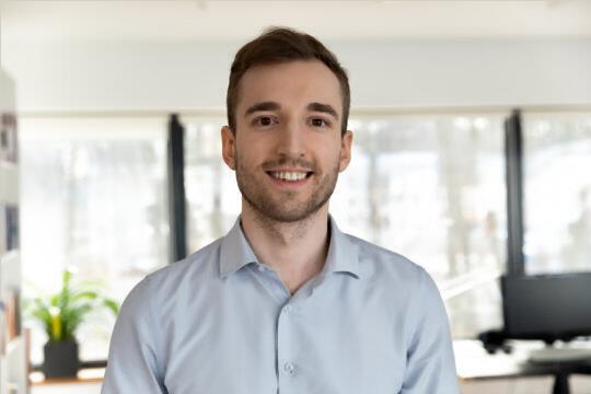 Portrait of young smiling handsome bearded man in glasses looking at camera chatting with wife friend by videocall. Millennial male team leader organize virtual meeting workshop with employees online